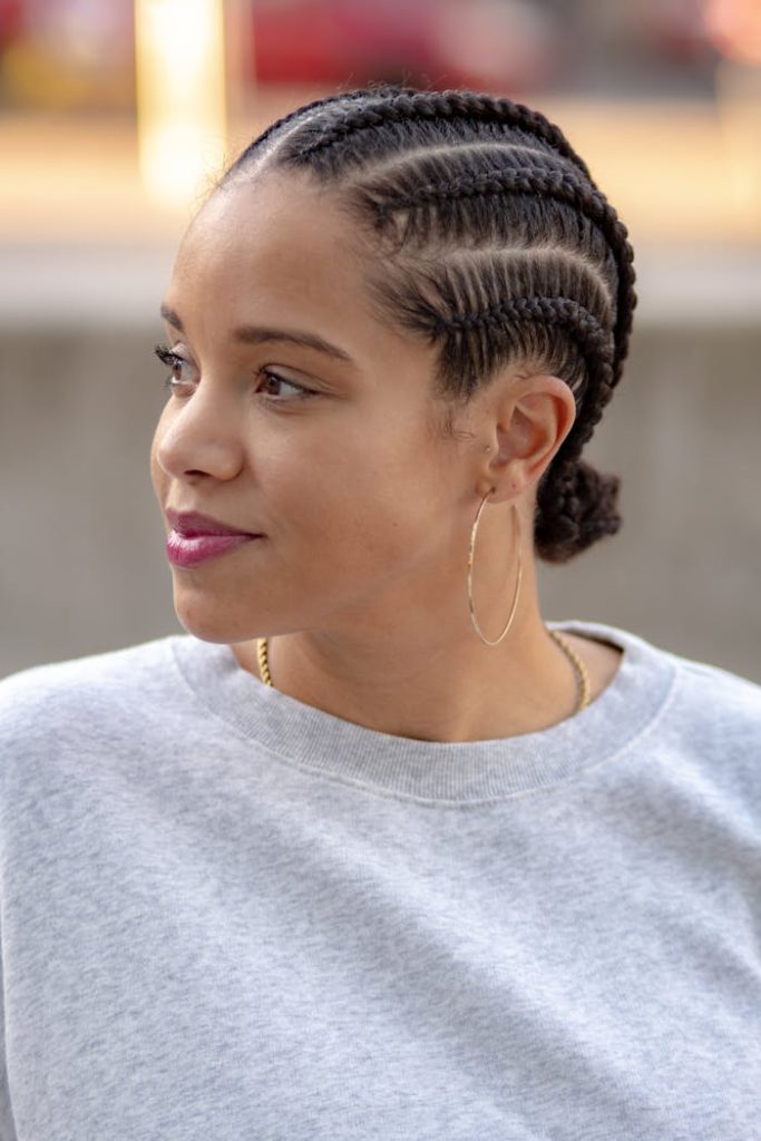 pexels-photo-6163386-1 A woman with braided hair and loop earrings gazes afar, wearing a gray sweater outdoors.
